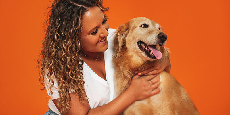 A woman smiling and looking at a golden retriever that she's hugging